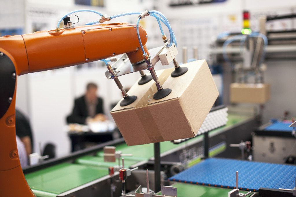 A robotic arm uses suction cups to hold up a box in a factor